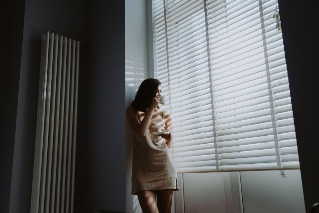 Person quietly holding a warm cup of coffee by a window during an ordinary morning routine