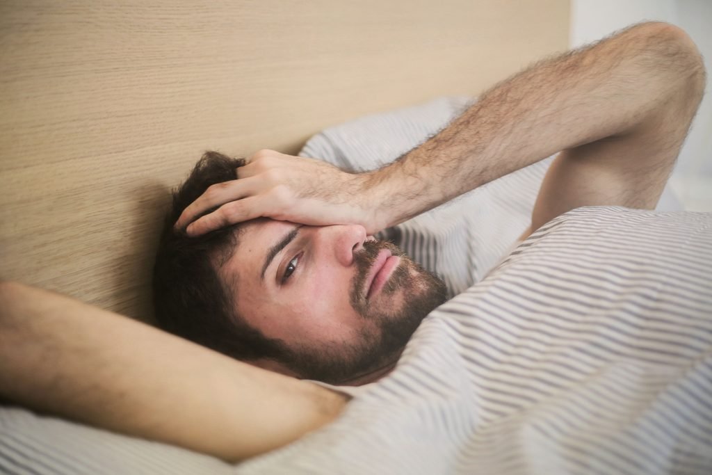 Man lying awake in bed covering his face, feeling groggy after waking up