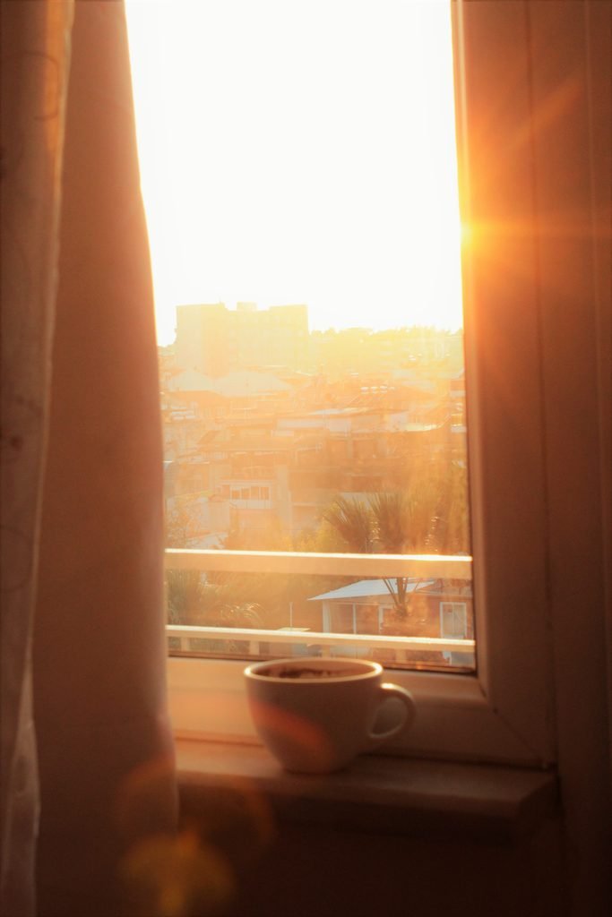Cup of coffee on a sunlit windowsill overlooking the city at sunrise