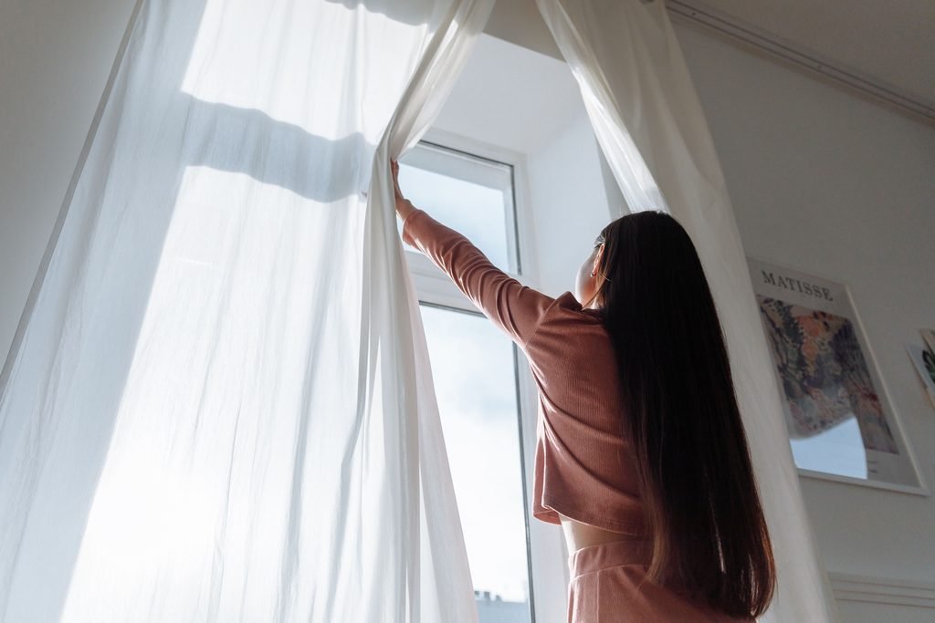 Woman opening bedroom curtains to let morning sunlight in
