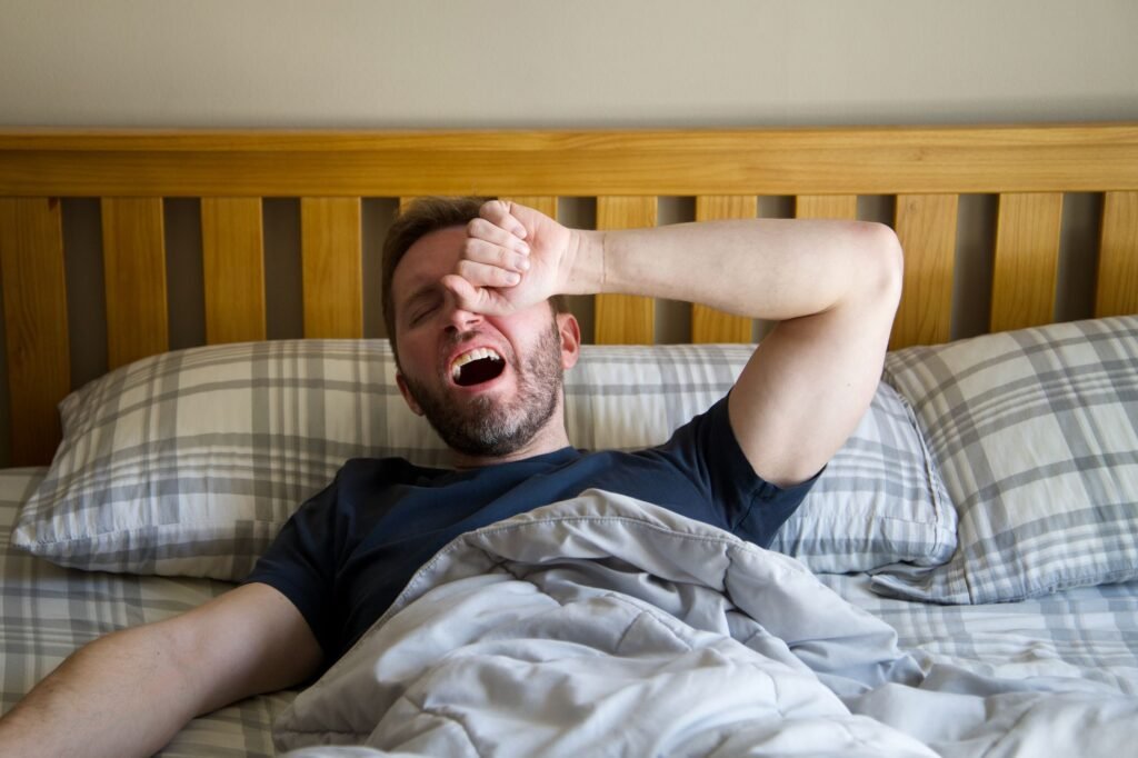 Woman sitting on the edge of her bed in the morning looking tired despite a full night's sleep