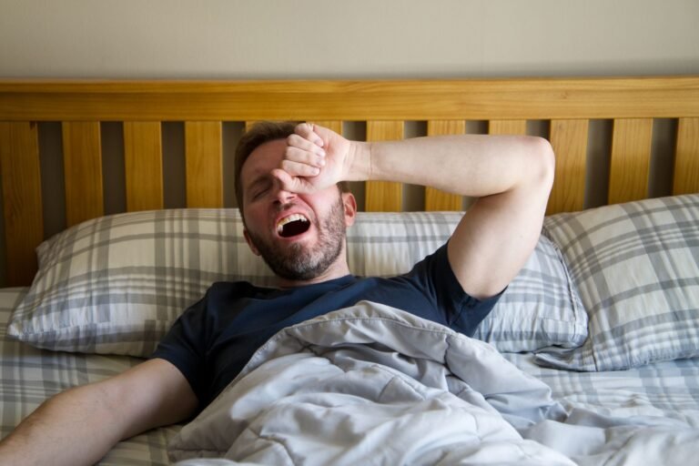 Woman sitting on the edge of her bed in the morning looking tired despite a full night's sleep