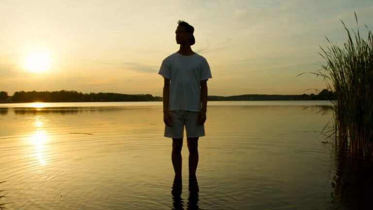 Person standing quietly at a crossroads path during sunrise, symbolizing searching for direction in life