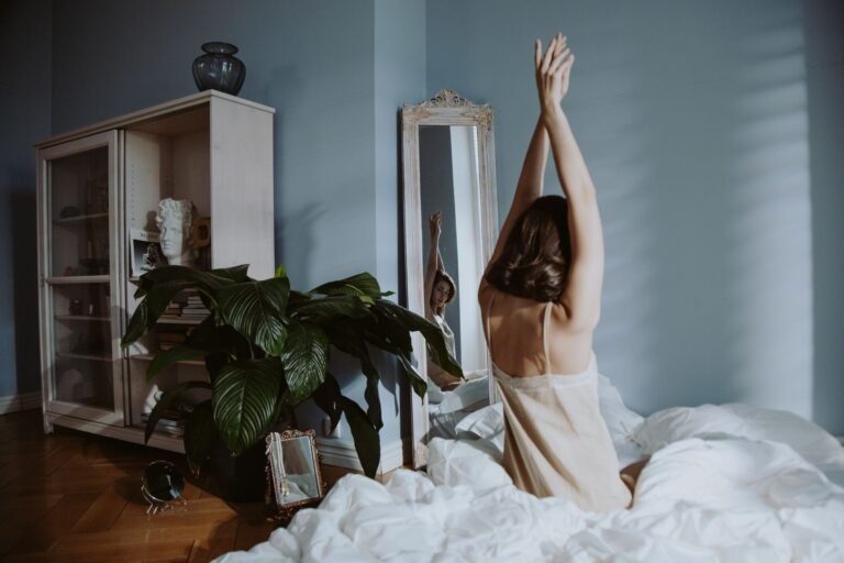 Person gently stretching in soft morning light beside their bed
